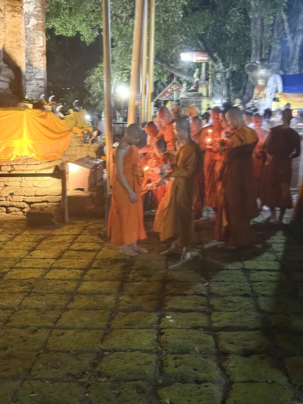 Barefoot monks and novices holding lit candles on the laterite paving at Wat Jed Yod at night, before the wian tian procession