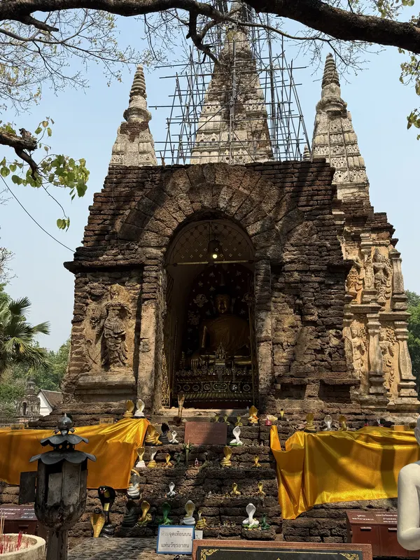 The brick shrine niche of Wat Chet Yot with a golden Buddha and saffron cloth, the seven-spired stupa in scaffolding behind, Jed Yod, Chiang Mai