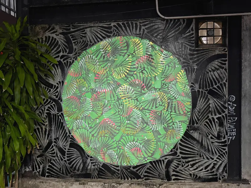 A circular green mural of fanning leaf shapes on a black fan-patterned wall, beside a leafy plant